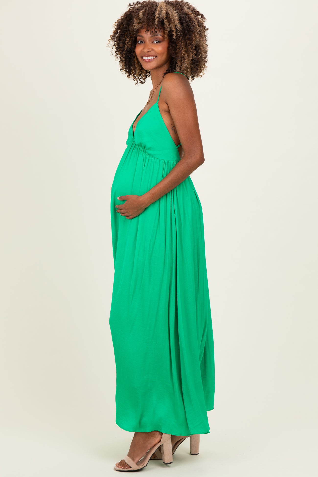woman wearing a green maternity maxi dress with a fitted bodice and flowing skirt, showing her baby bump