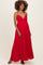 woman wearing a red maxi maternity dress with a gathered bust and spaghetti straps, showcasing her baby bump