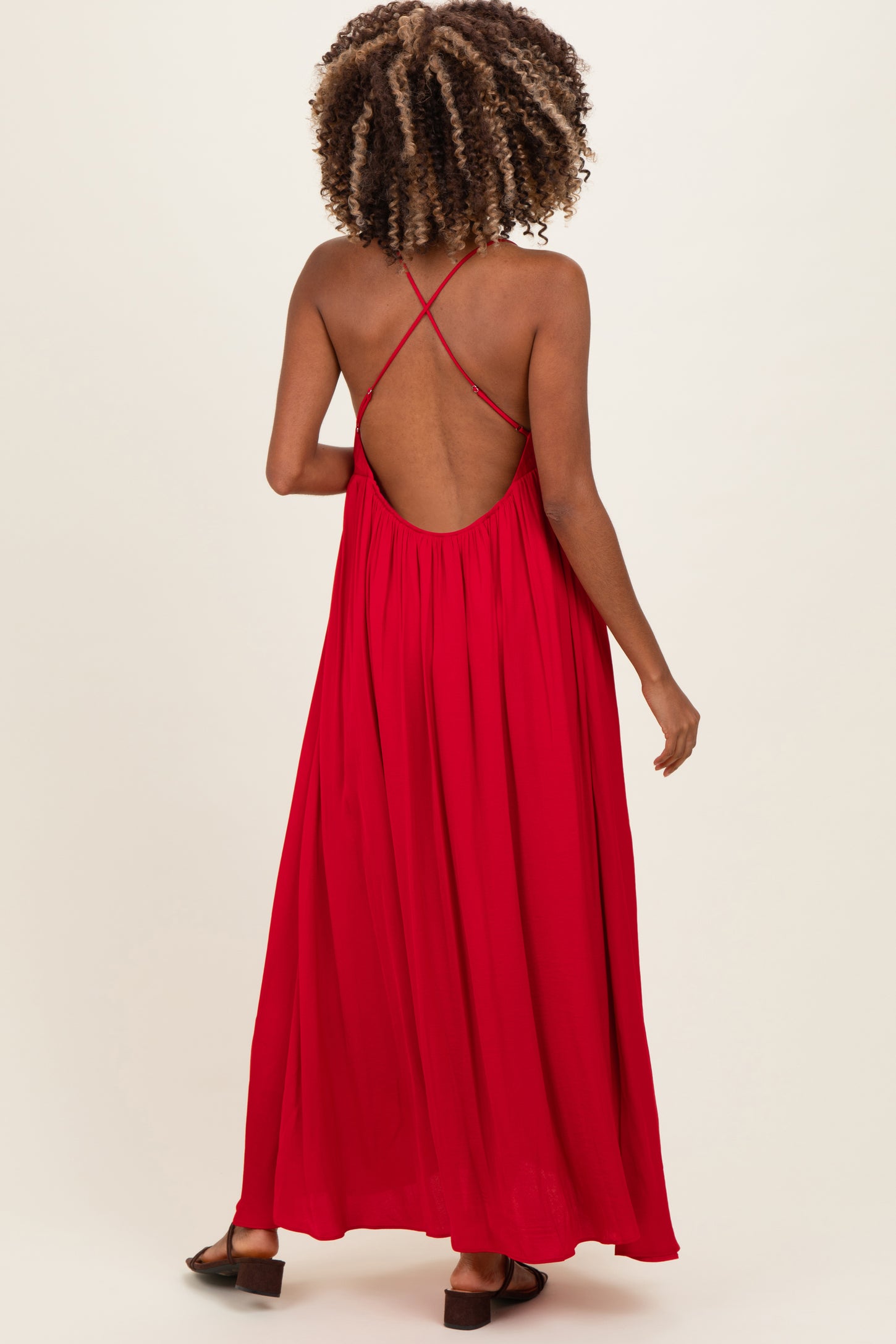 woman wearing a flowing red maternity maxi dress with a crisscross back design