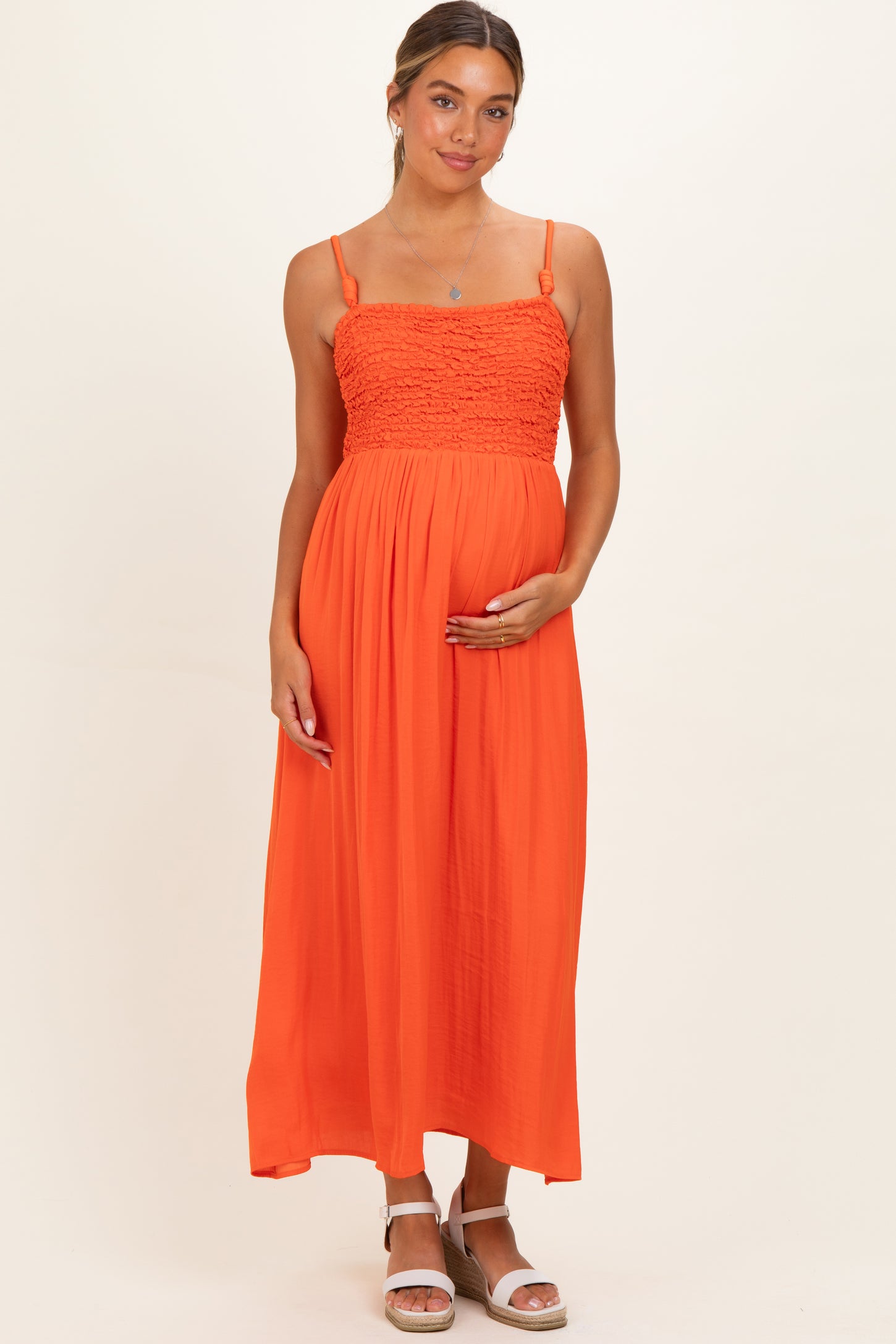 woman wearing an orange maternity maxi dress with smocked bodice and holding her baby bump
