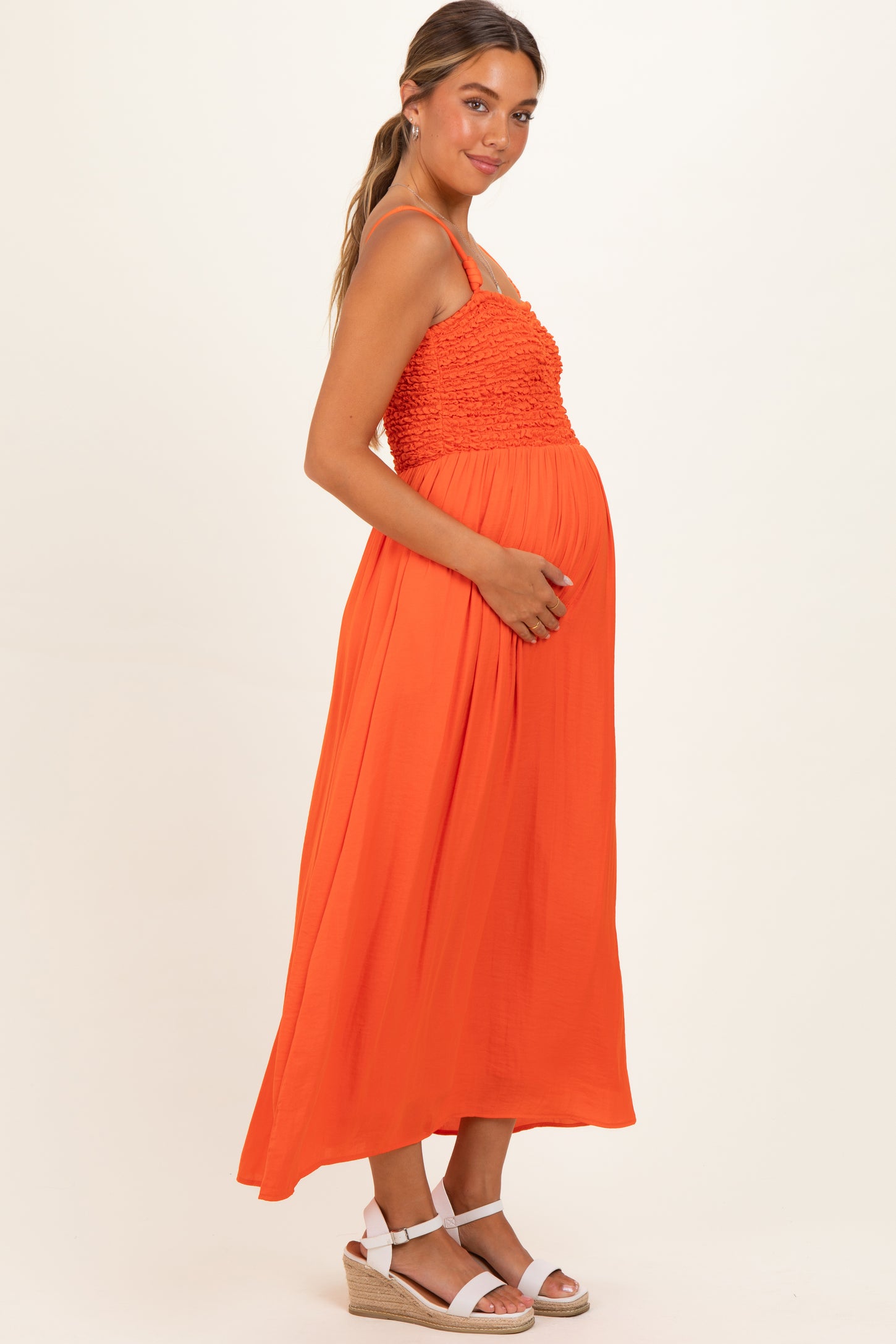 woman wearing an orange maternity maxi dress with a smocked bodice and holding her baby bump
