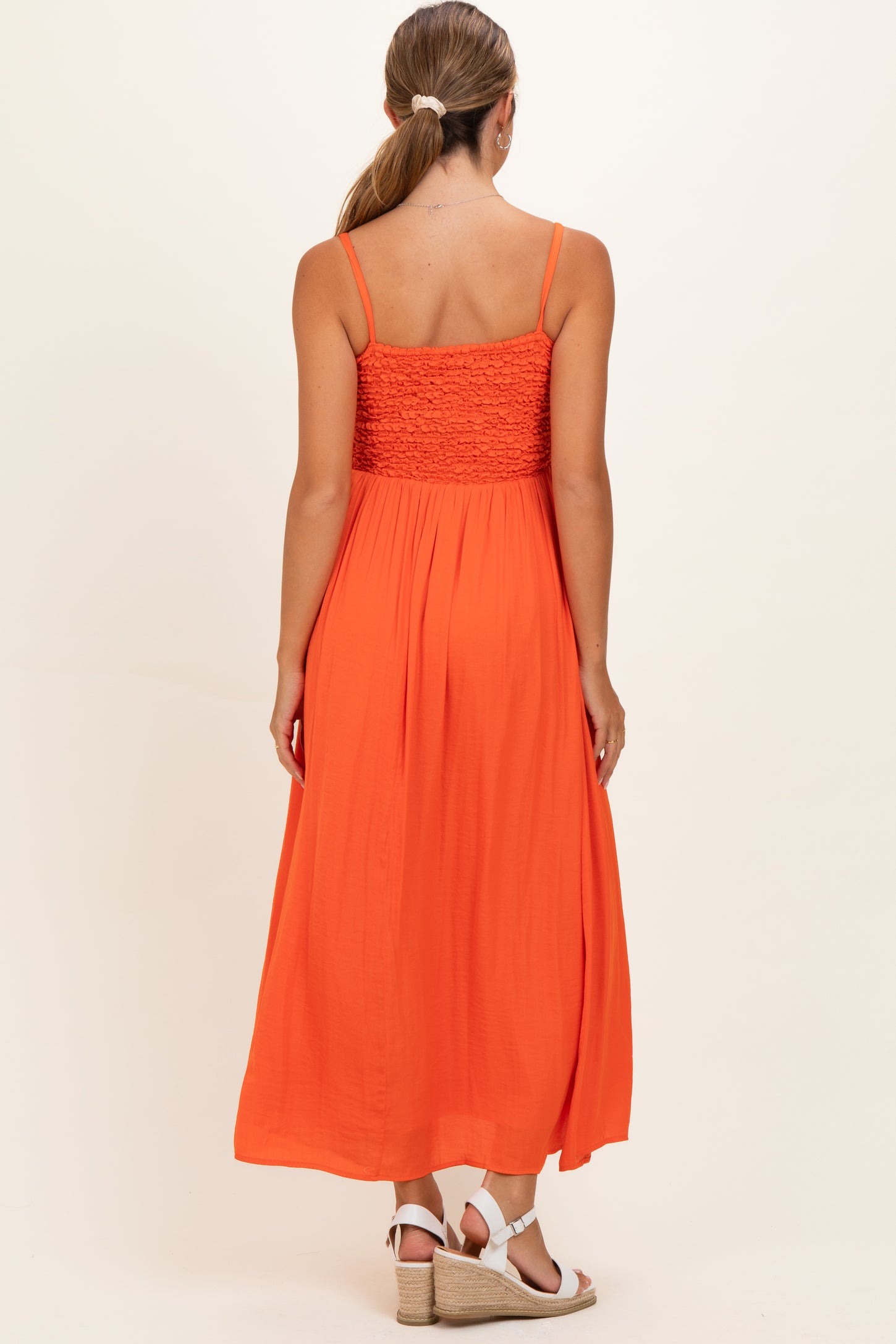 woman wearing an orange maternity maxi dress with smocked bodice and thin straps, showing the back view