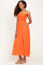 woman wearing a bright orange maxi dress with smocked bodice and adjustable straps, standing with one hand in pocket