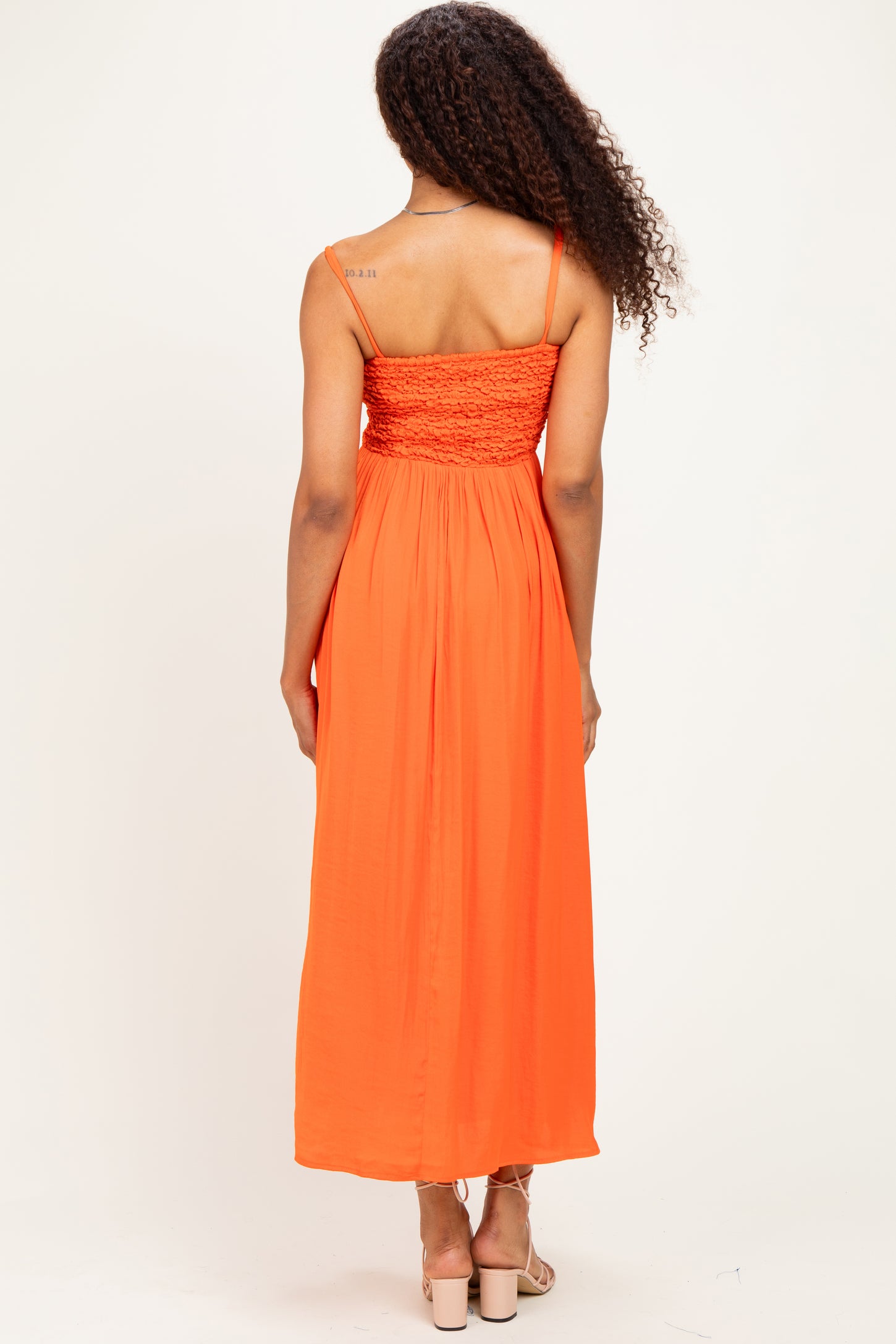 woman wearing an orange maxi dress with a smocked bodice and adjustable straps, shown from the back