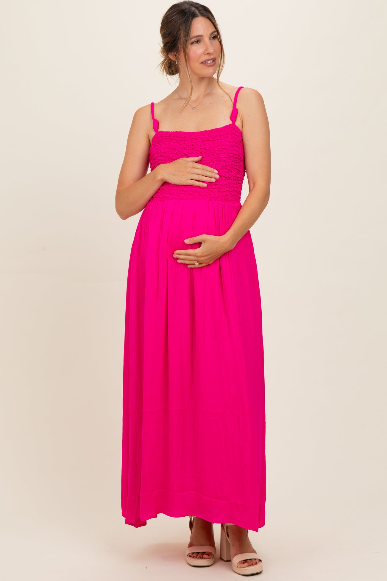 woman wearing a bright pink maternity maxi dress with smocked bodice and holding her baby bump