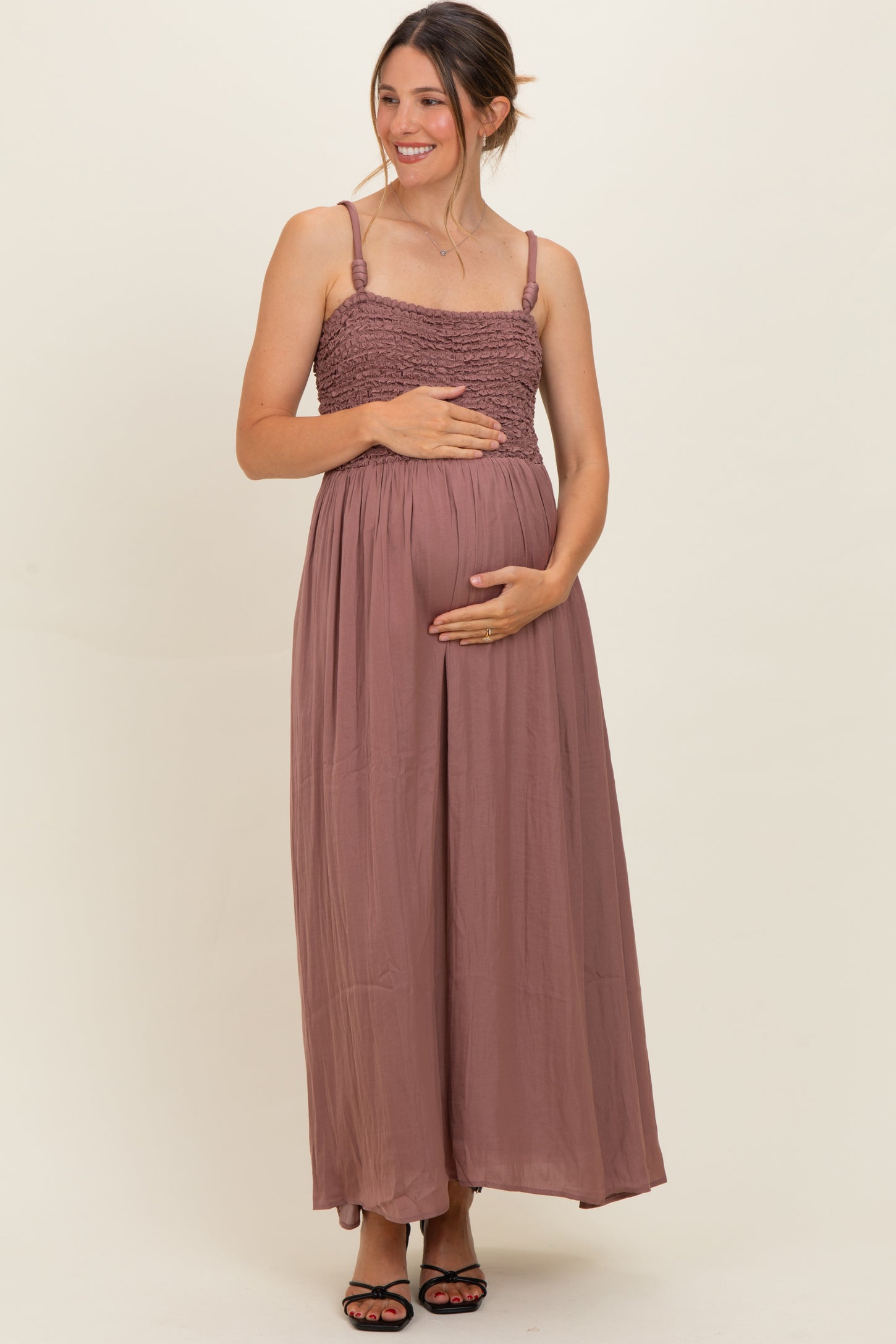 woman wearing a mauve maternity maxi dress with a smocked bodice, cradling her baby bump
