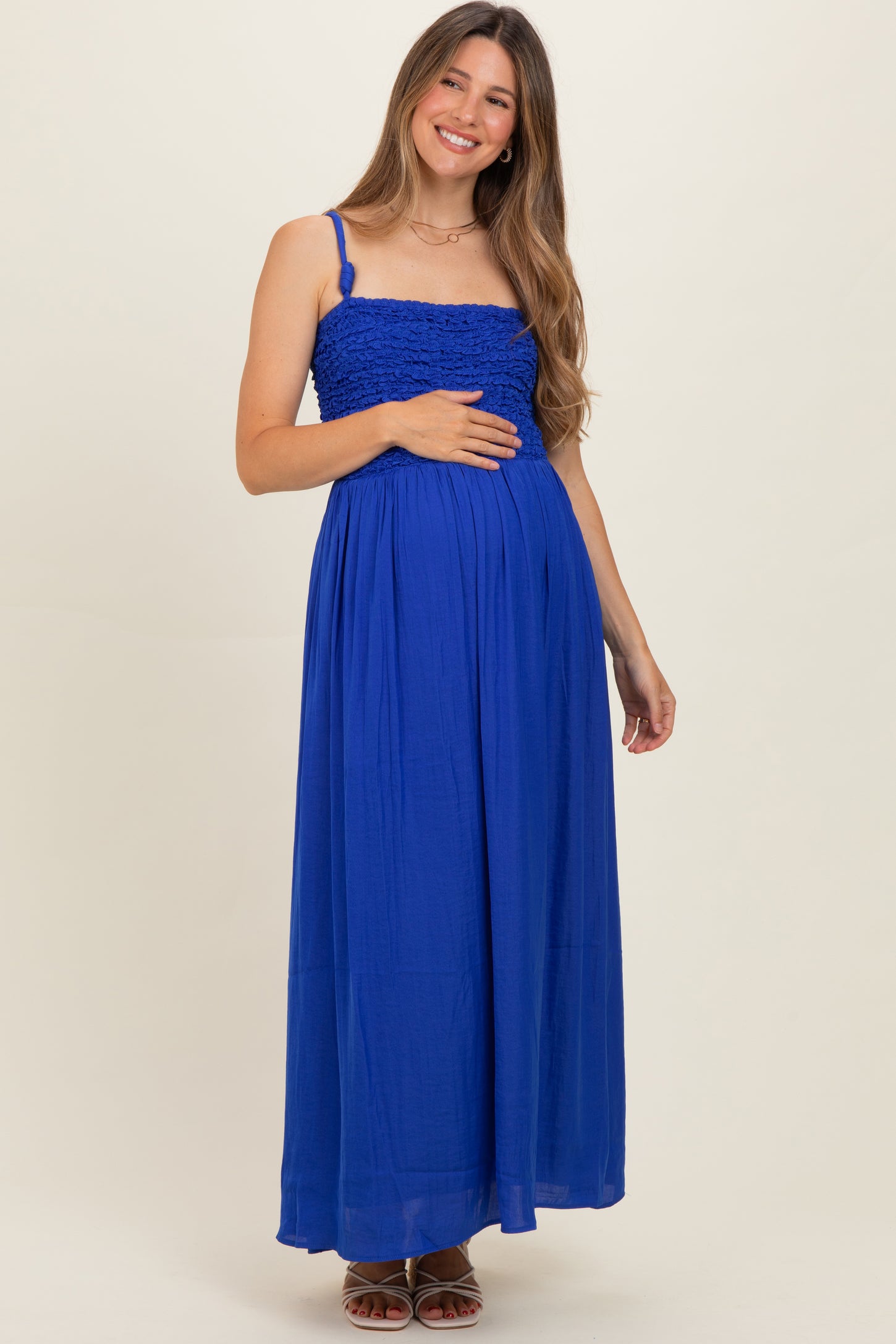 woman wearing a bright blue maternity maxi dress with a smocked bodice and holding her baby bump
