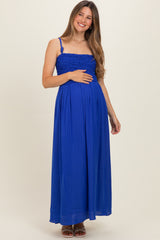 woman wearing a bright blue maternity maxi dress with a smocked bodice and holding her baby bump