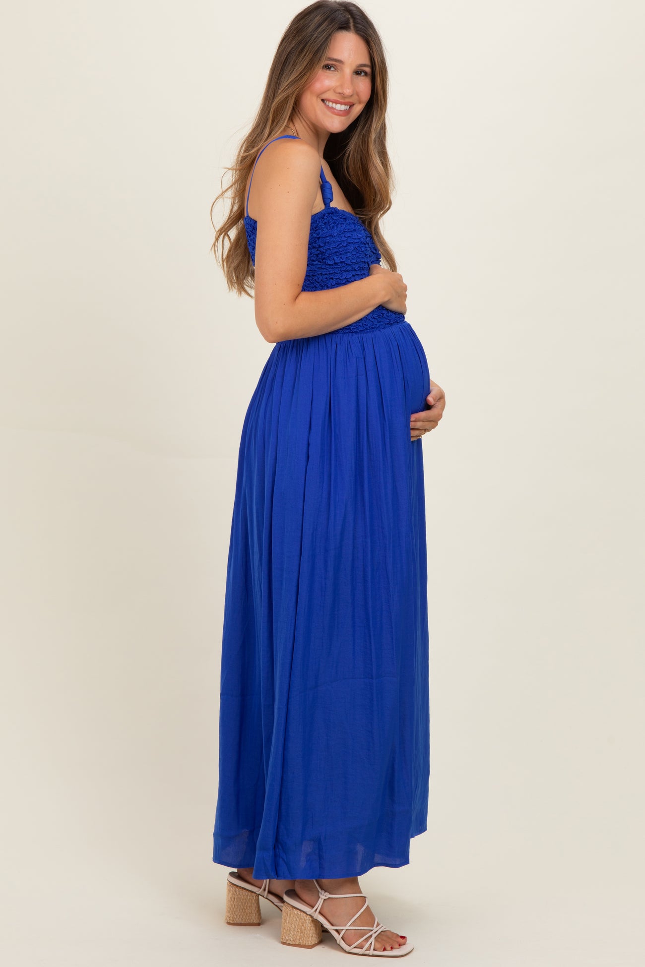 woman wearing a blue maternity maxi dress with smocked bodice and holding her baby bump