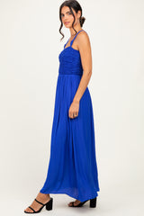 woman wearing a bright blue maxi dress with a smocked bodice and thin straps, standing sideways with black block heels