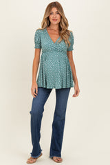 woman wearing a teal maternity top with white polka dots and puff sleeves, paired with flared jeans and showing her baby bump