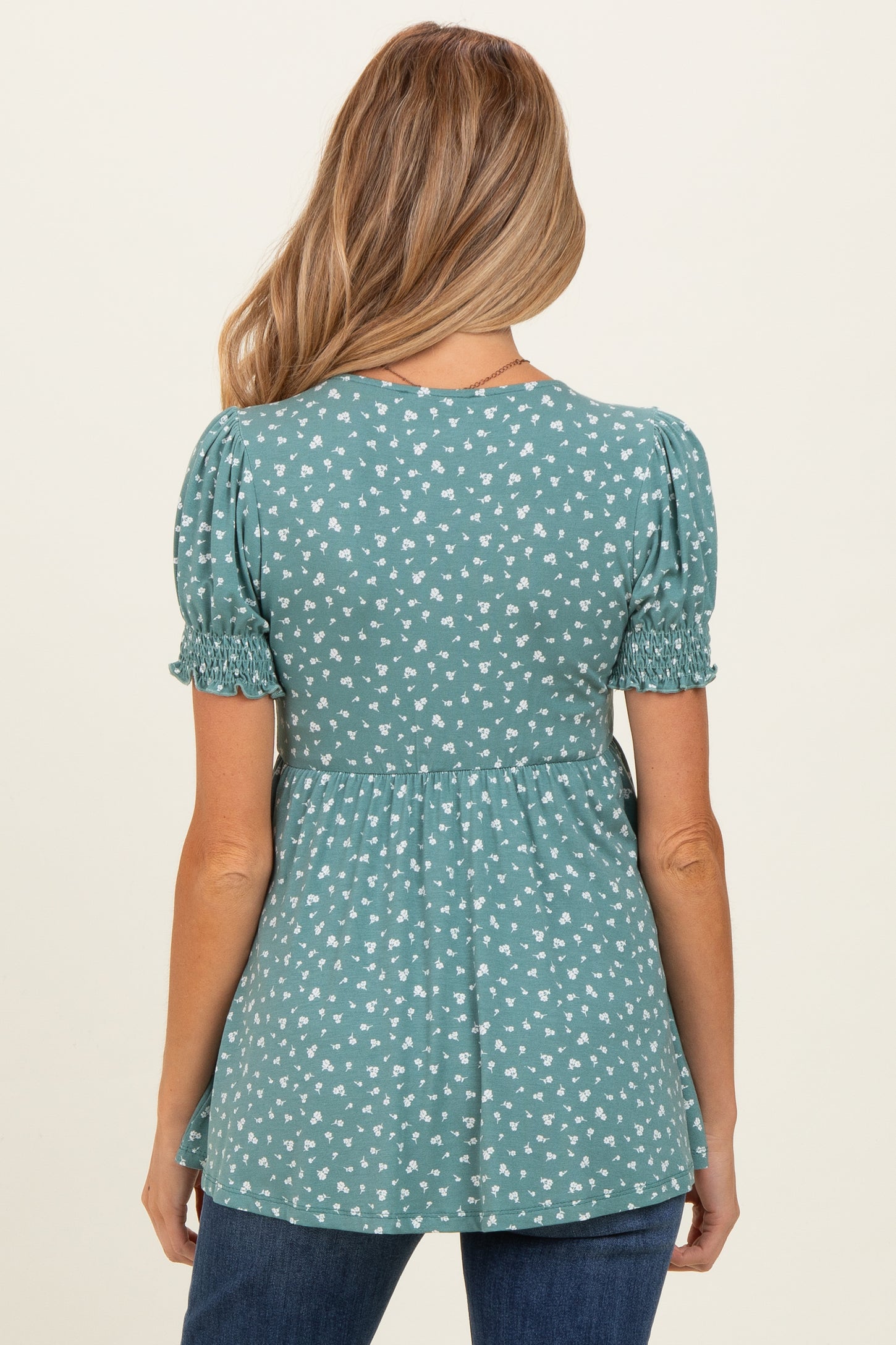 woman wearing a teal maternity top with puff sleeves and a floral print, showing a baby bump from the back