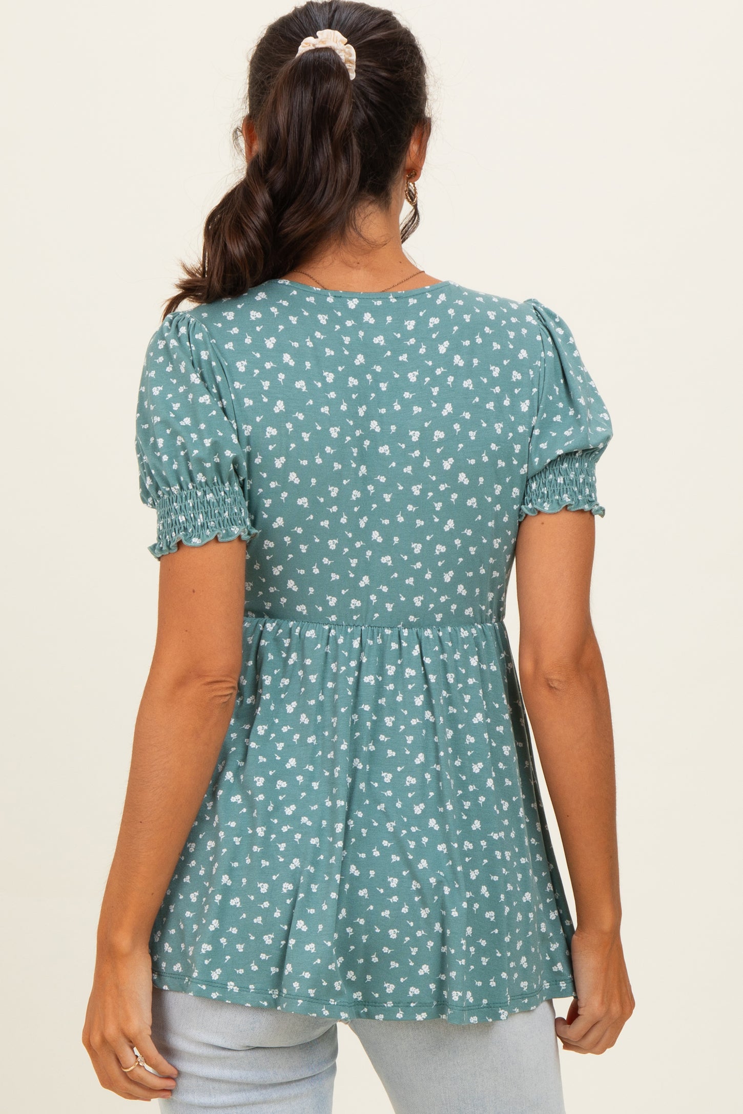woman wearing a teal peplum top with small white floral print and puff sleeves, shown from the back