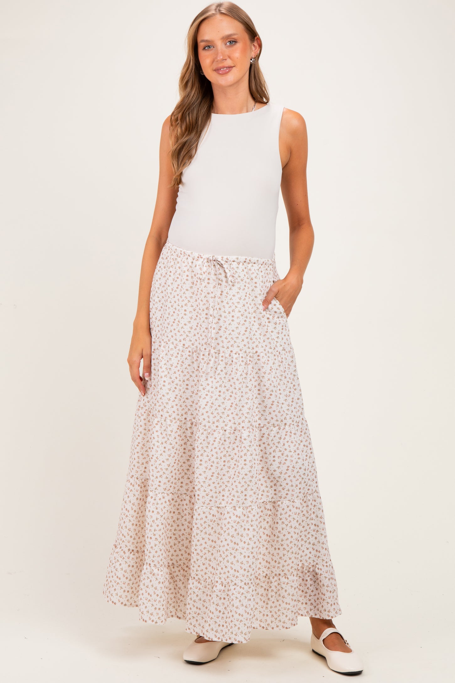 woman wearing a white sleeveless top and a floral printed maxi skirt with pockets, styled for maternity wear