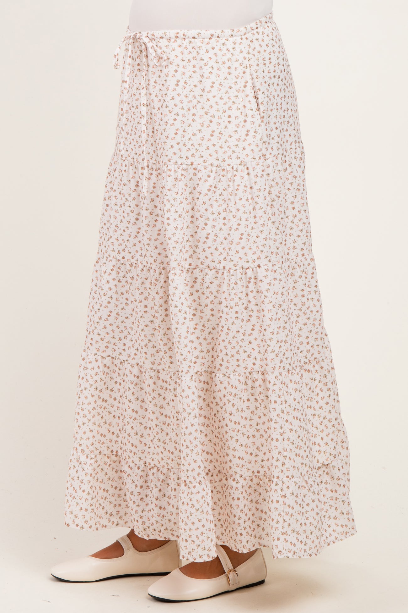 maternity wear white tiered maxi skirt with a floral print and side pockets, styled with a tied waist and a model wearing it