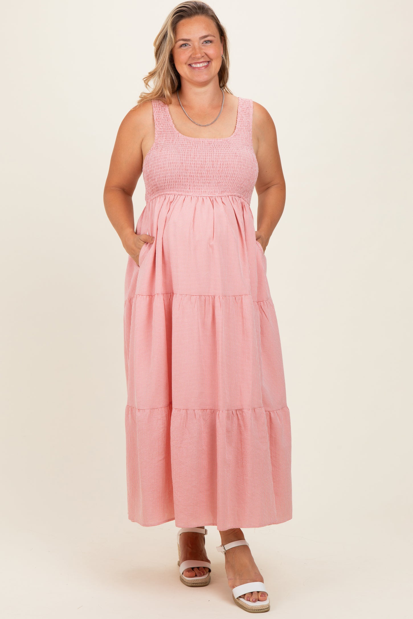 woman wearing a pink striped maternity plus maxi dress with a smocked bodice and pockets, smiling at the camera