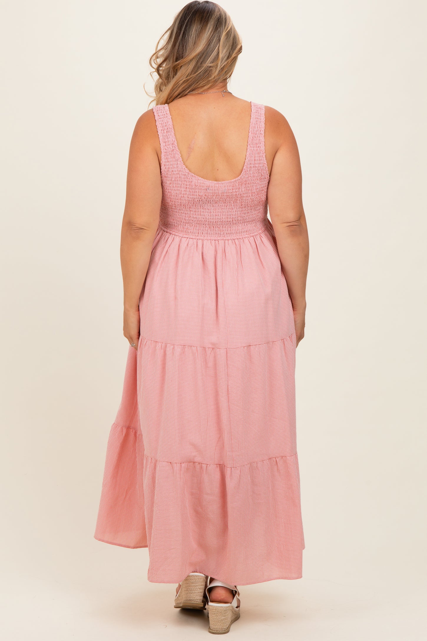woman wearing a pink tiered maternity maxi dress with a smocked bodice, showcasing her baby bump from the back