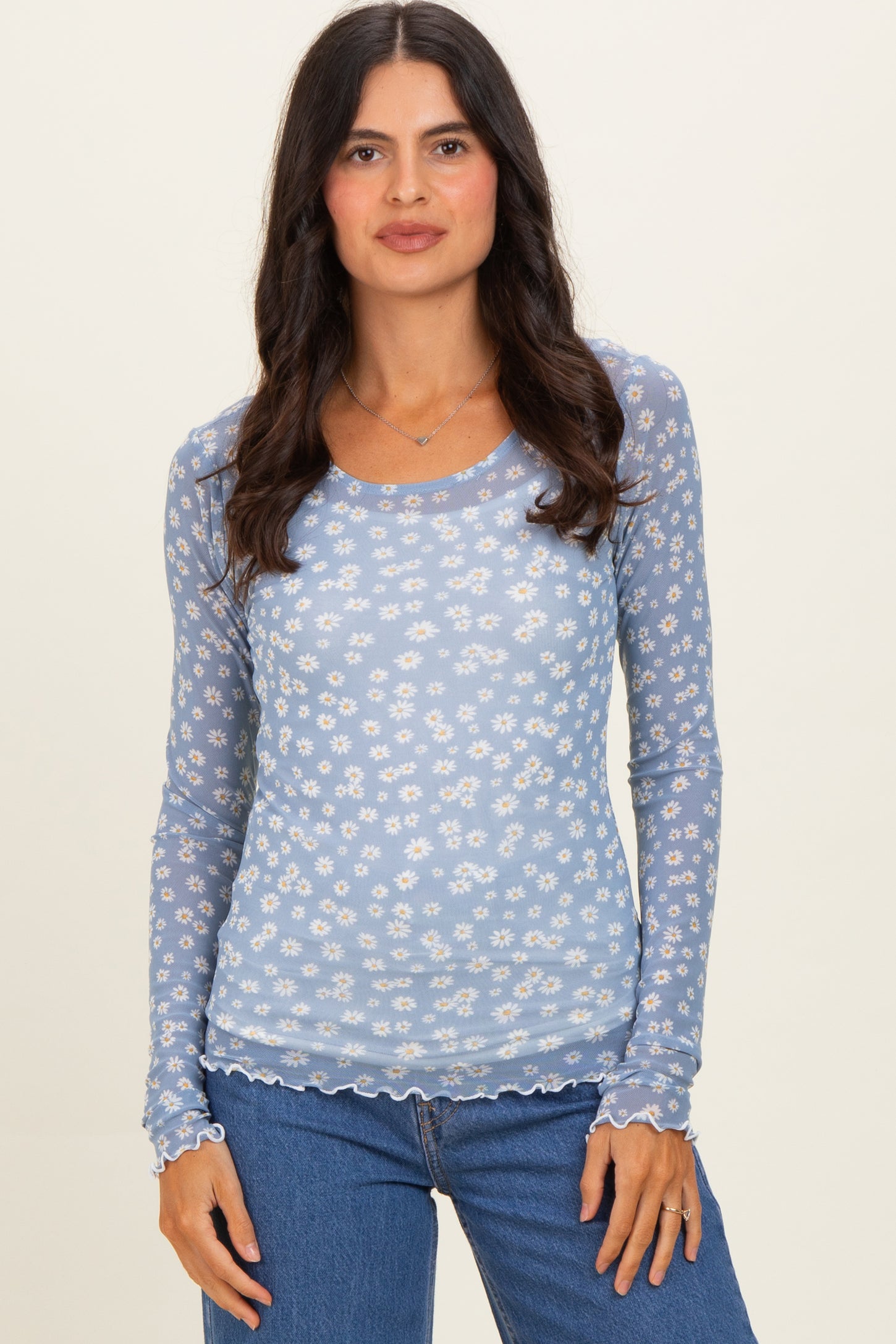 woman wearing a light blue long sleeve top with a white floral pattern and scalloped hem, paired with blue jeans