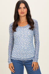 woman wearing a light blue long sleeve top with a white floral pattern and scalloped hem, paired with blue jeans
