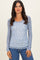 woman wearing a light blue long sleeve top with a white floral pattern and scalloped hem, paired with blue jeans