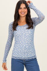 woman wearing a light blue long sleeve floral top with scalloped edges and fitted style