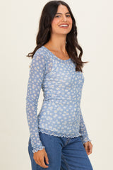 woman wearing a light blue long sleeve top with a floral print and scalloped edges, styled with high-waisted jeans