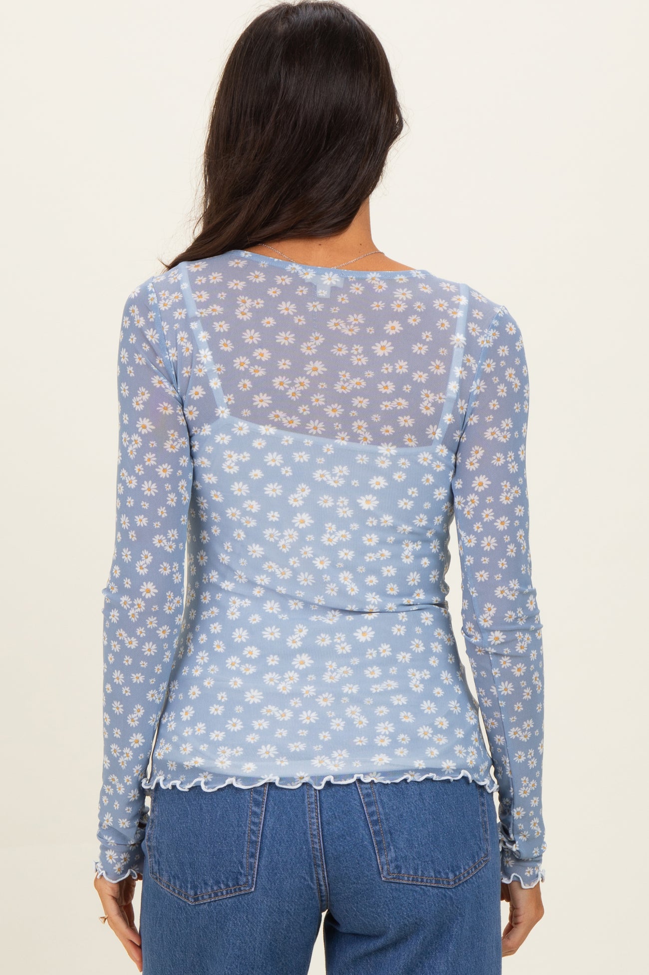woman wearing a light blue floral sheer long sleeve top with scalloped hem and back design
