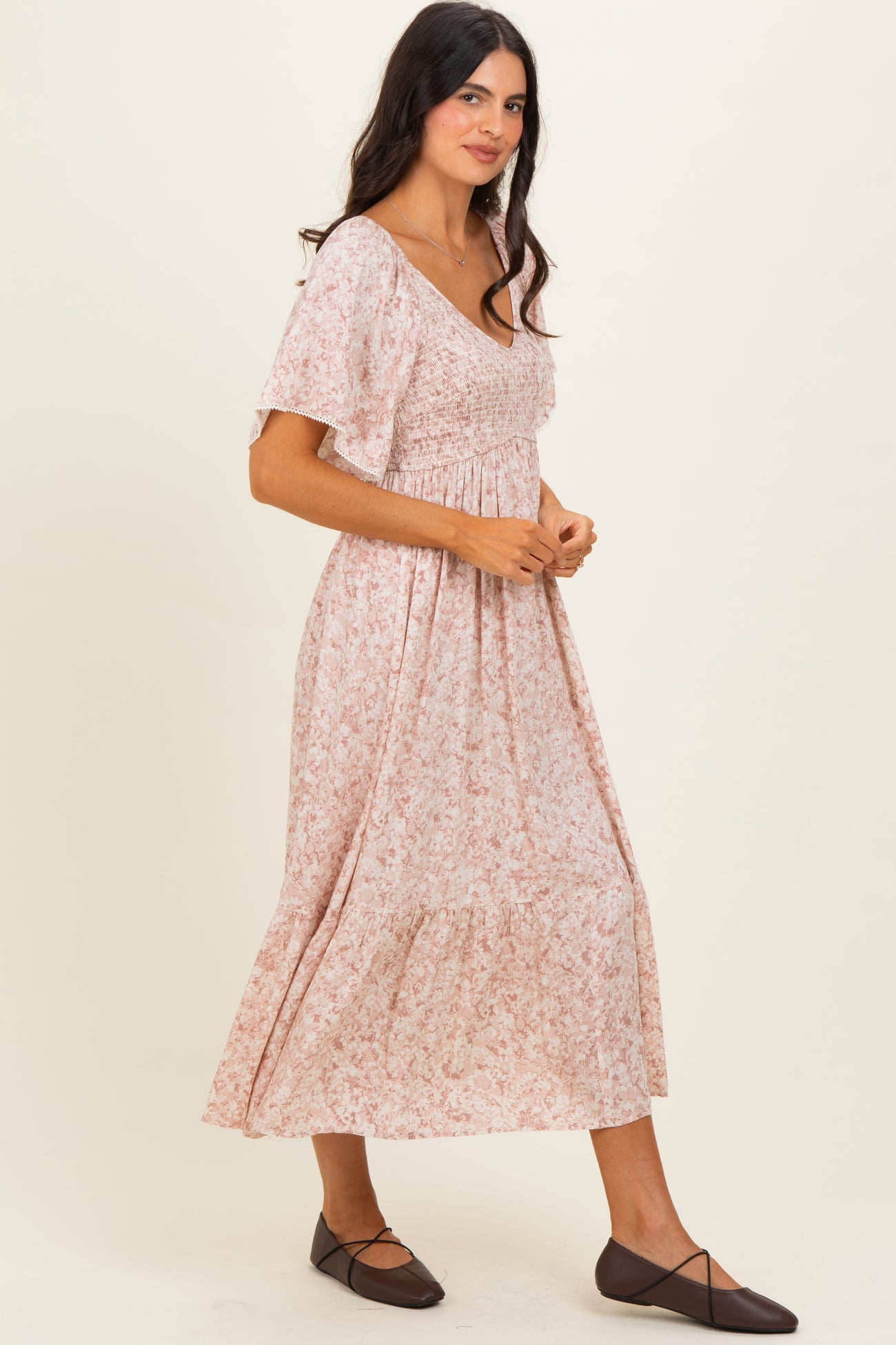 woman wearing a pink floral maxi dress with short sleeves and smocked bodice, standing sideways and smiling