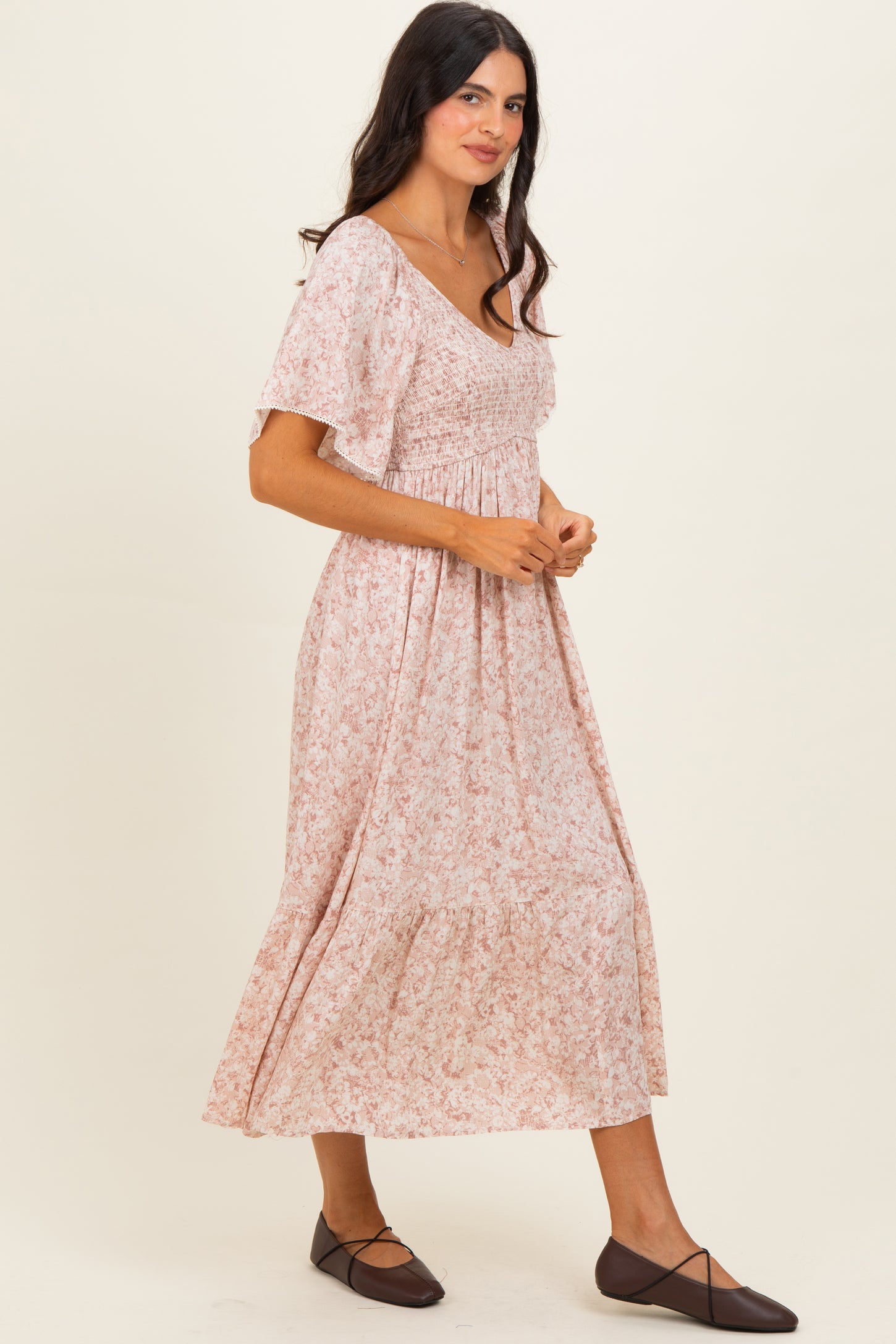 woman wearing a pink floral maxi dress with short sleeves and smocked bodice, standing sideways and smiling