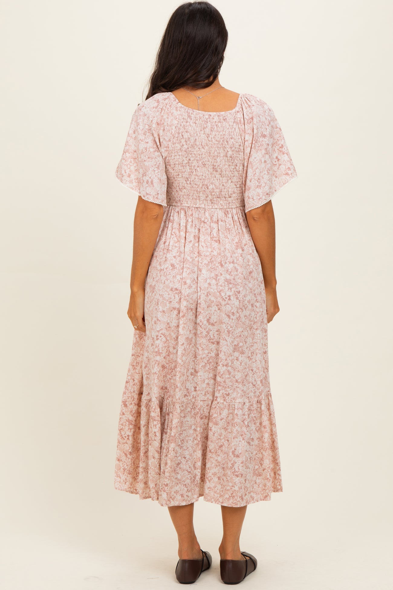 woman wearing a pink floral midi dress with short flutter sleeves and a smocked bodice, seen from the back