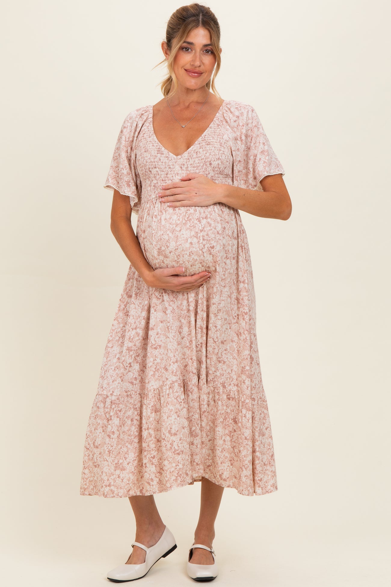 woman wearing a pink floral maternity dress and holding her baby bump