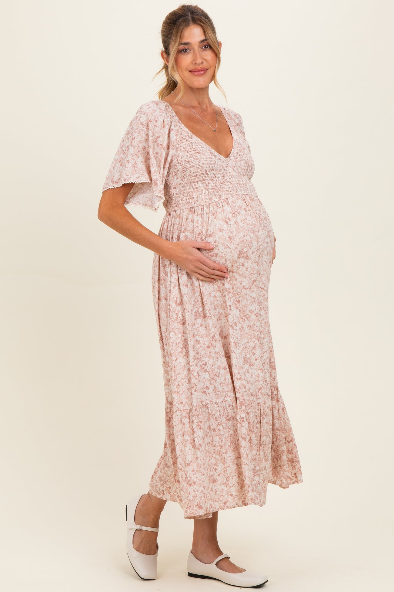 woman wearing a pink floral maternity dress with a smocked bodice and a baby bump visible
