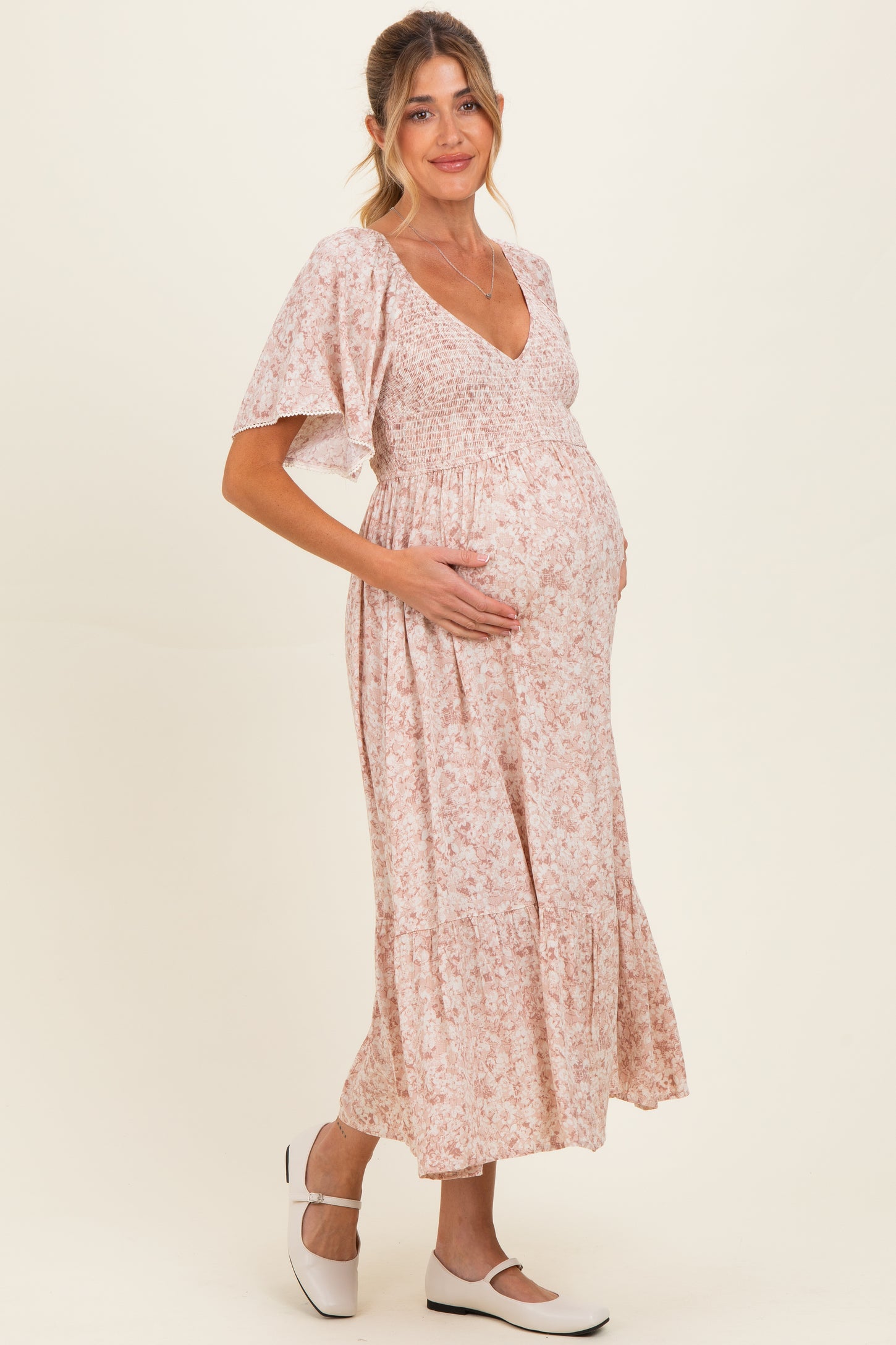 woman wearing a pink floral maternity dress with a smocked bodice and a baby bump visible