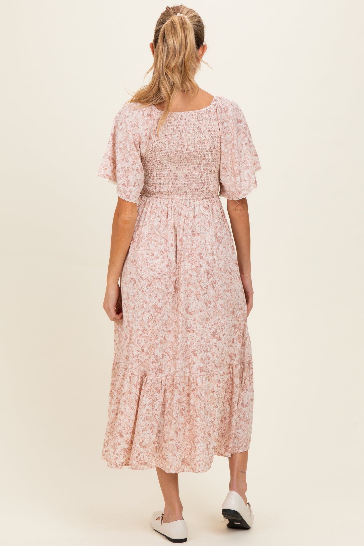 woman wearing a pink floral maternity dress with a smocked bodice and flutter sleeves, showing the back view