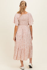 woman wearing a pink floral maternity dress with a smocked bodice and flutter sleeves, showing the back view