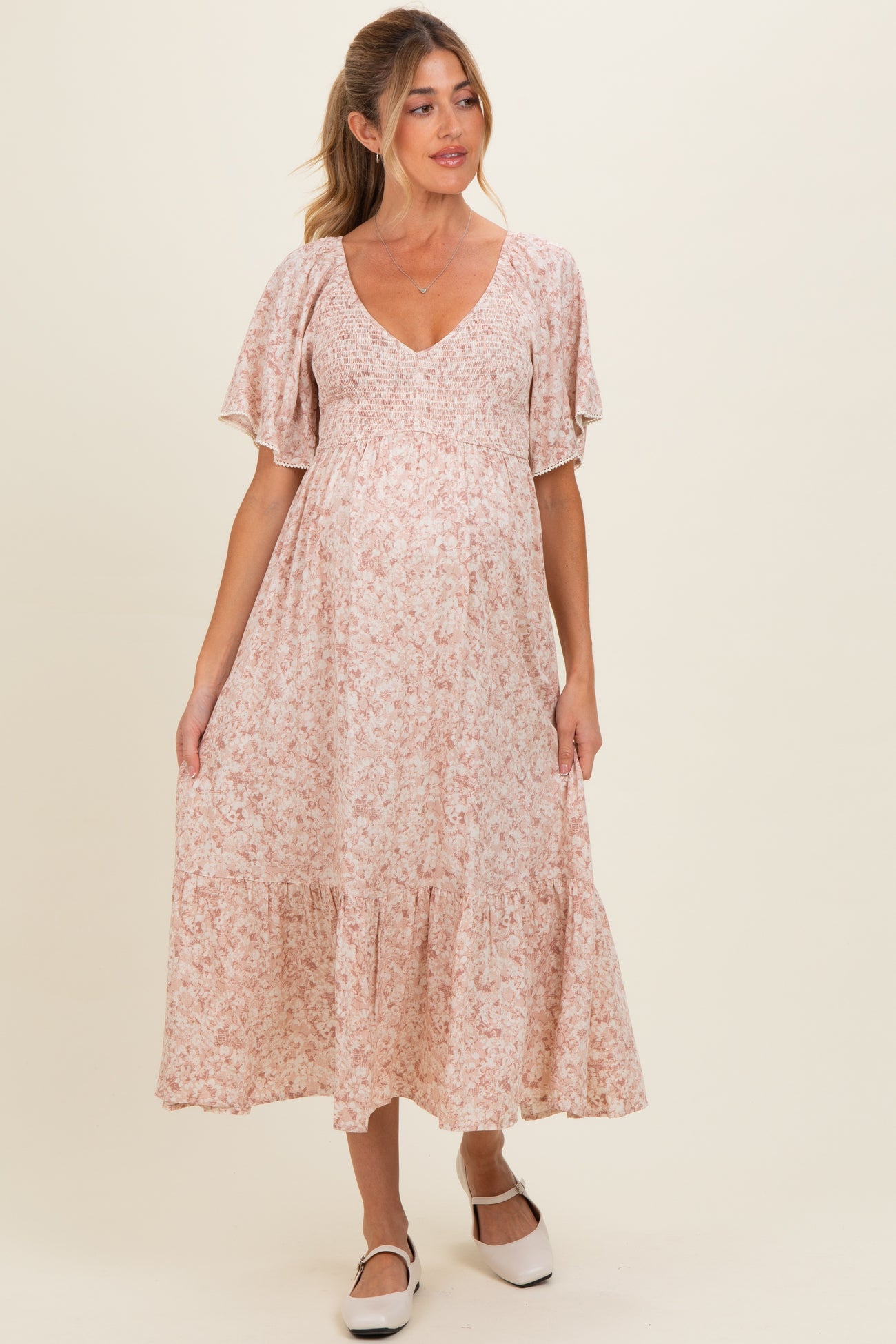woman wearing a floral pink maternity maxi dress with short flutter sleeves and a tiered hem, showing her baby bump