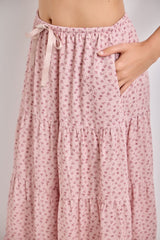 woman wearing a pink floral tiered maxi skirt with an elastic waistband and pockets, featuring a tie detail