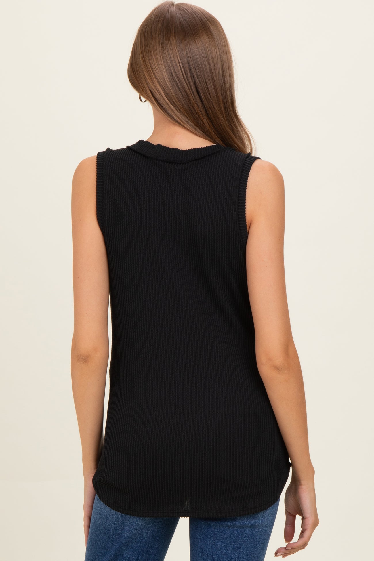 woman wearing a black sleeveless ribbed maternity top, viewed from the back, paired with blue jeans