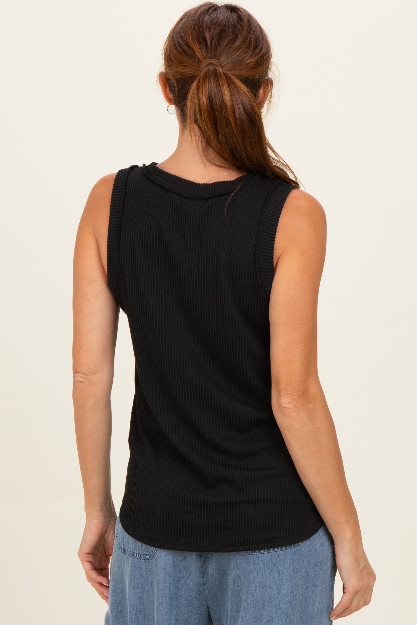 woman wearing a black ribbed sleeveless top, seen from the back, styled with light blue wide-leg jeans