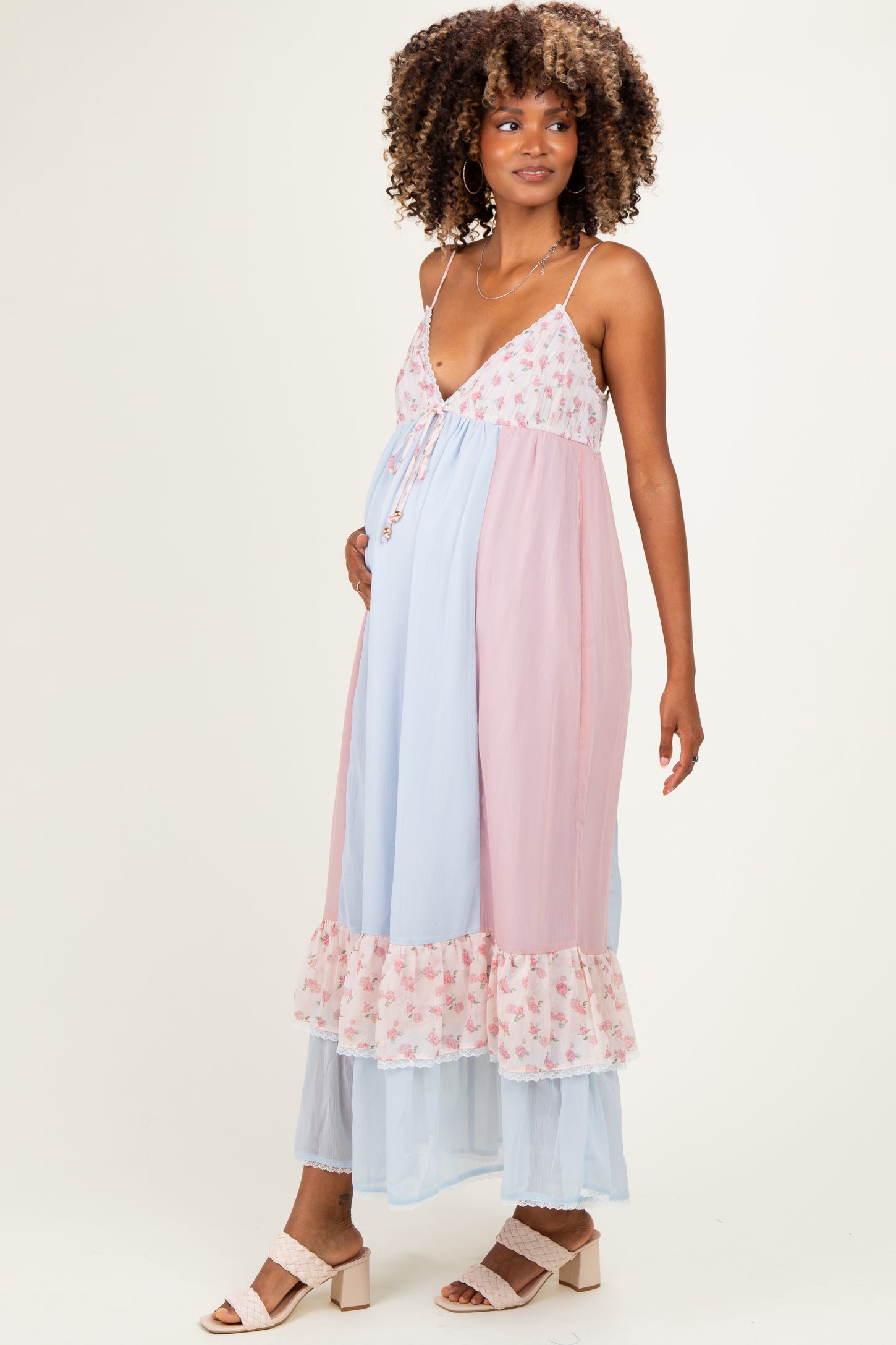 woman wearing a lightweight pastel pink and blue maternity dress with floral details and a ruffled hem, showing her baby bump