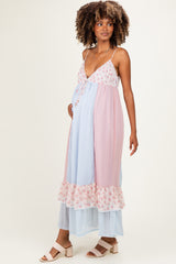 woman wearing a lightweight pastel pink and blue maternity dress with floral details and a ruffled hem, showing her baby bump