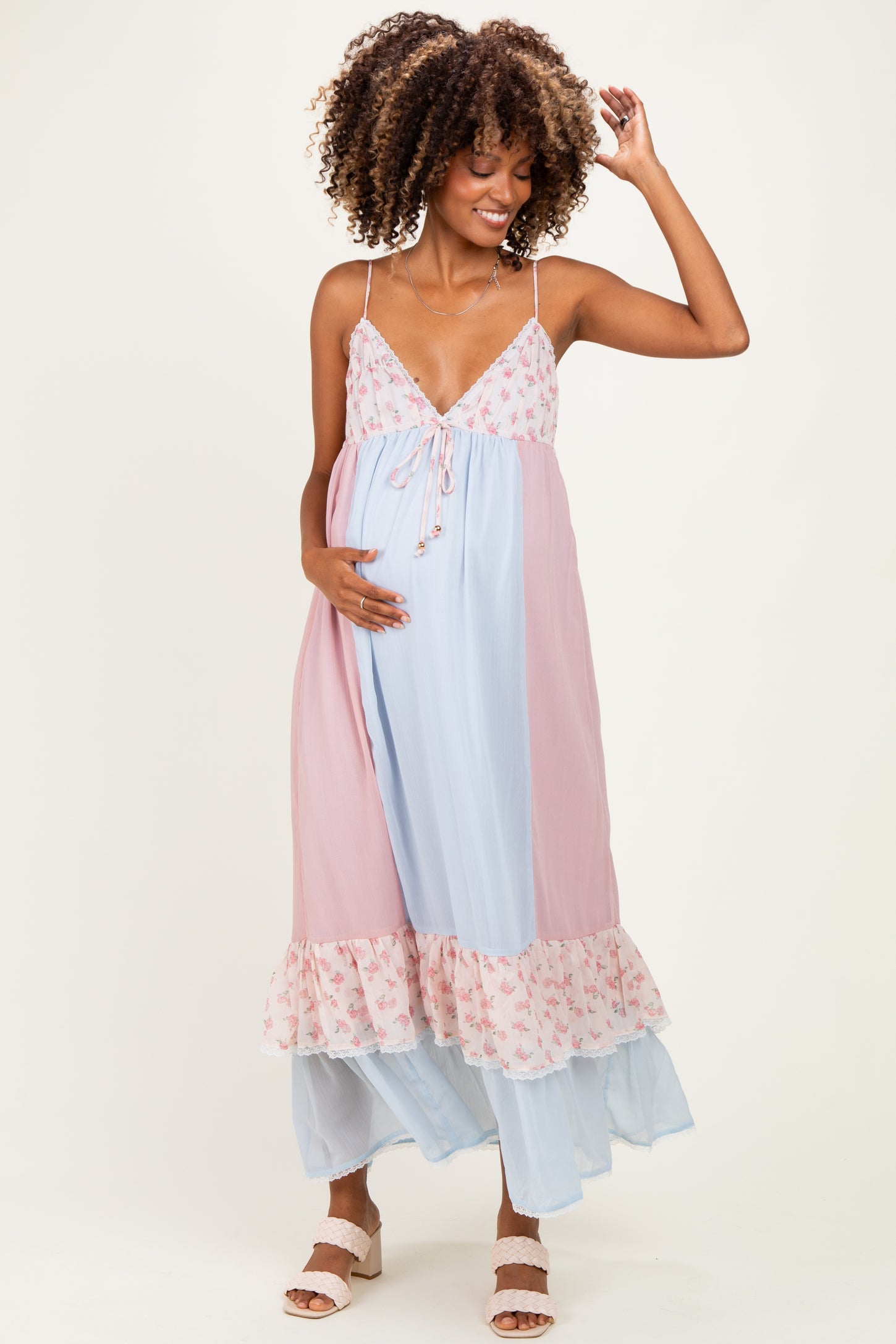 woman wearing a pink and blue floral maternity dress with spaghetti straps and ruffle hem, holding her baby bump