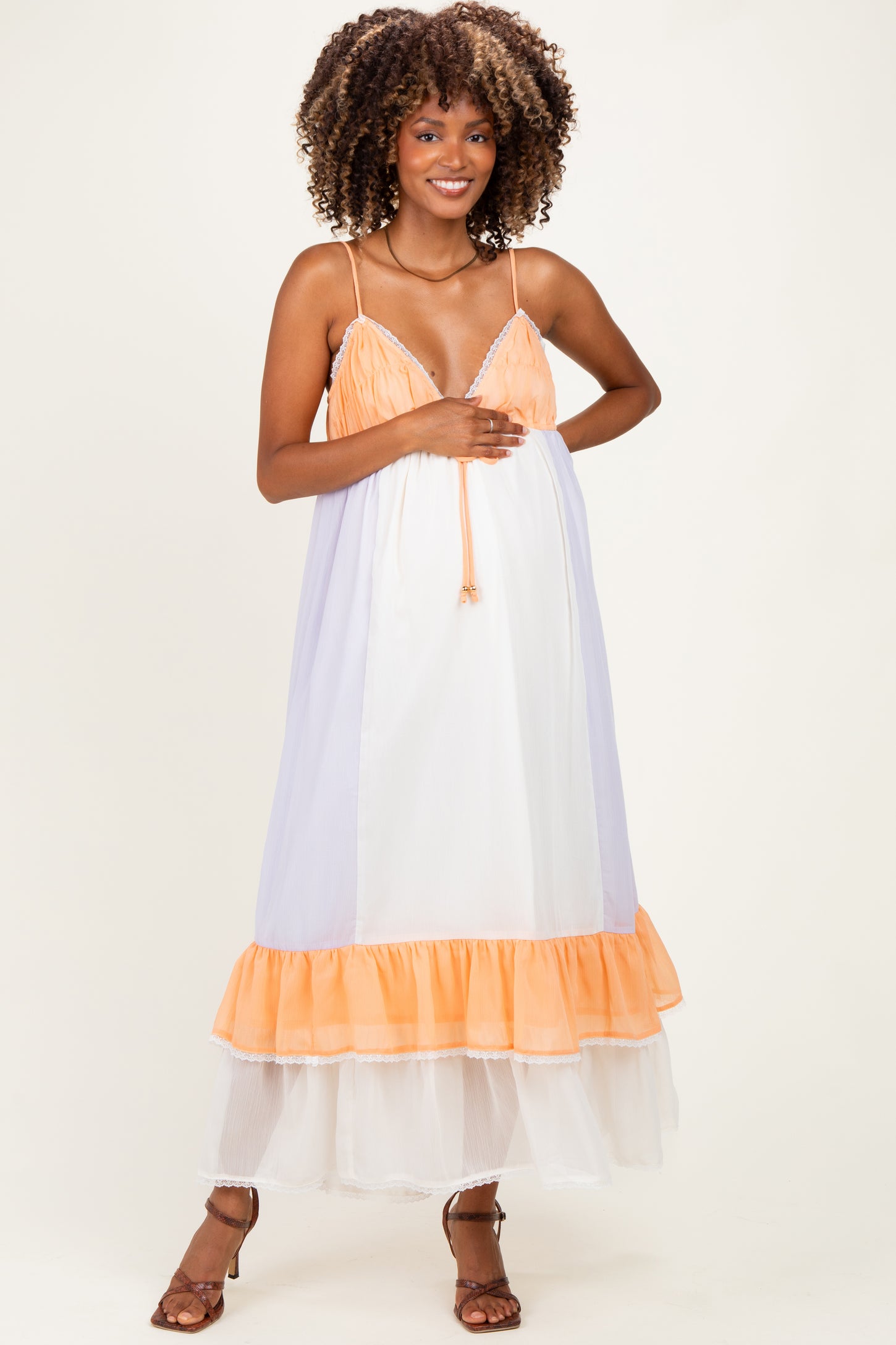 woman wearing a lavender and white maternity maxi dress with orange ruffle accents and a visible baby bump
