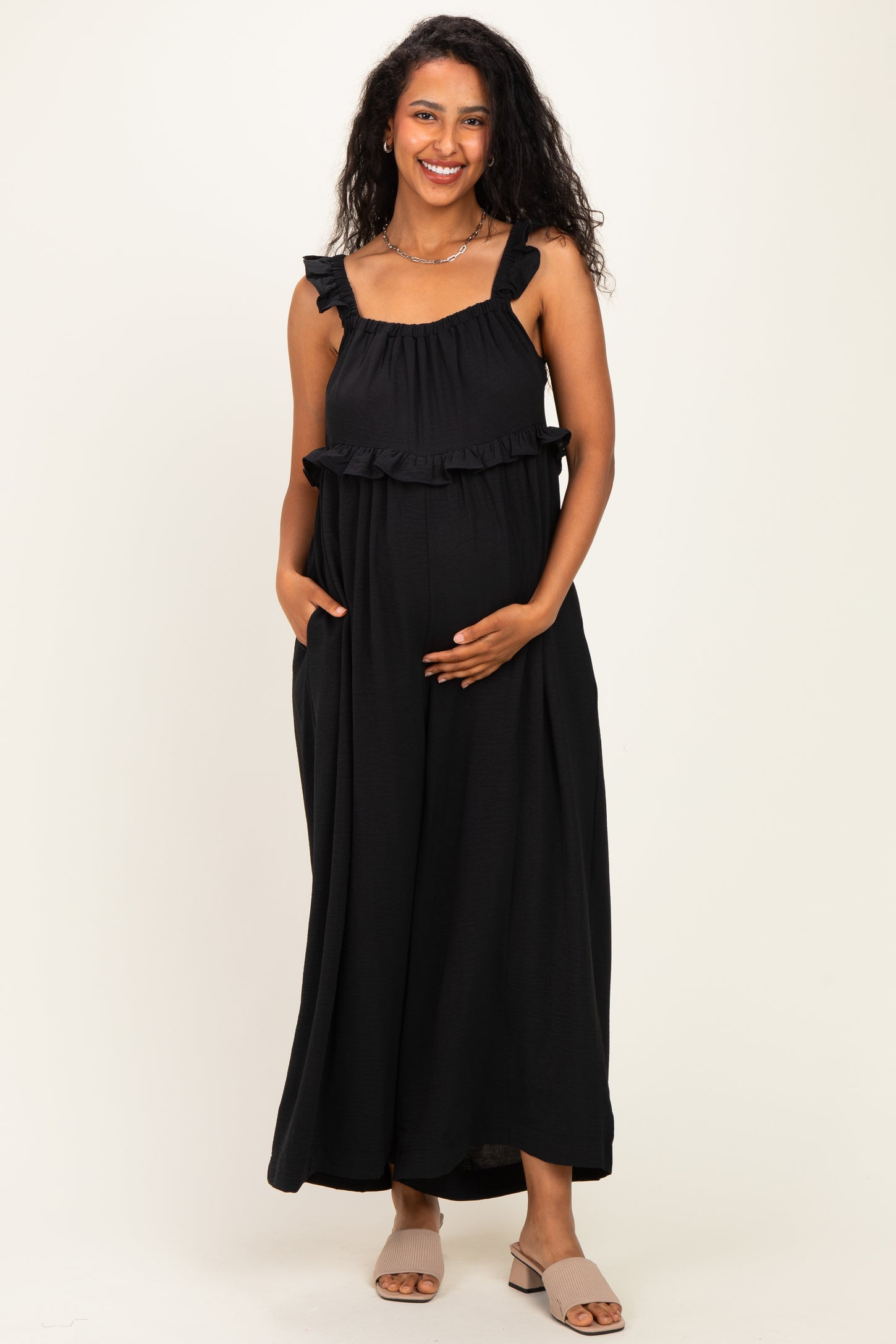 woman wearing a black maternity maxi dress with ruffled straps and holding her baby bump