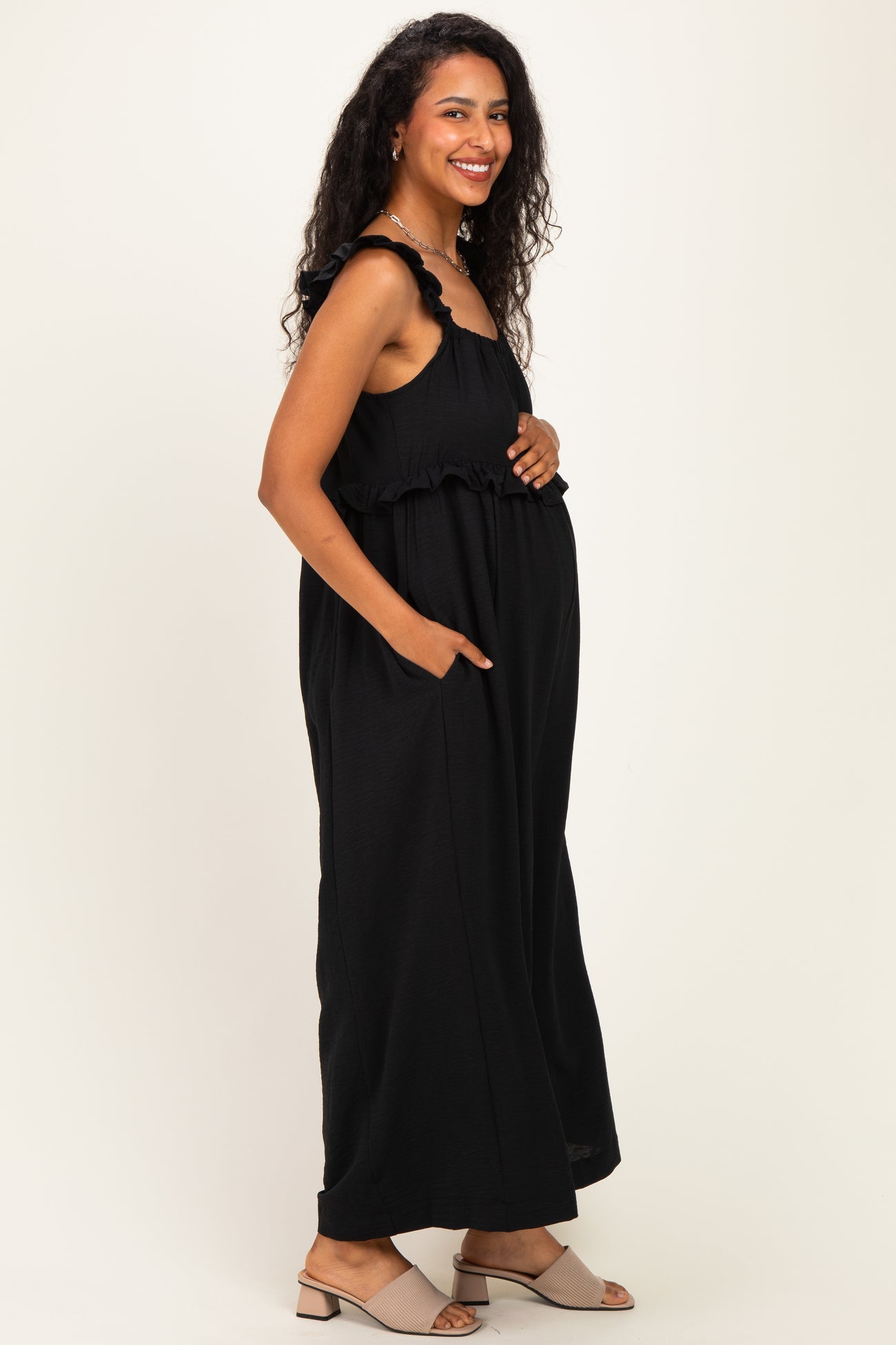 woman wearing a black maternity maxi dress with ruffle straps and pockets, showcasing her baby bump