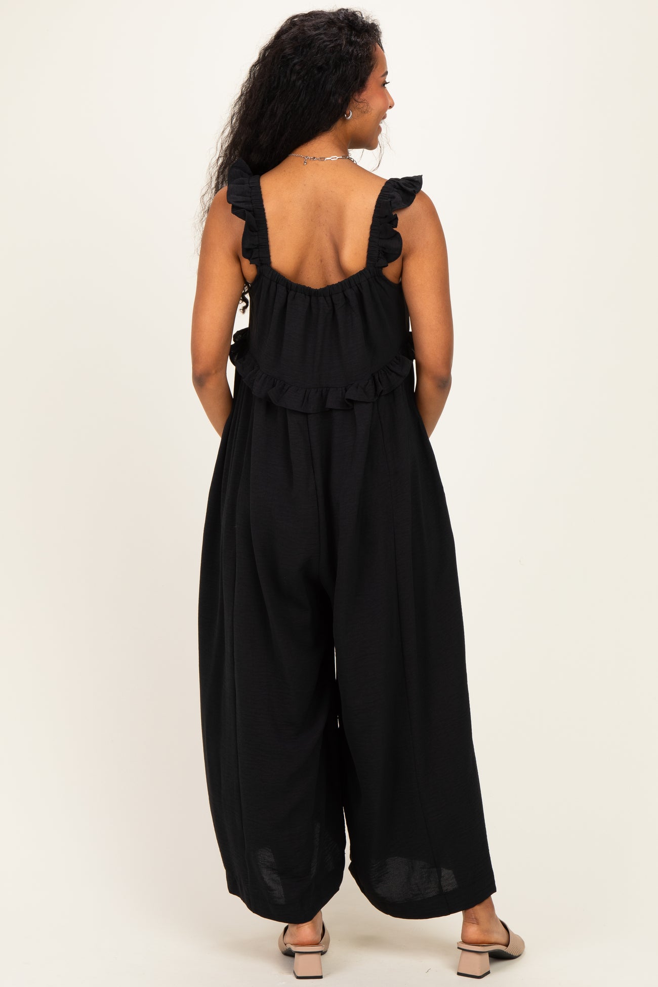 woman wearing a black maternity jumpsuit with ruffle straps and wide legs, showing a pregnant belly from the back