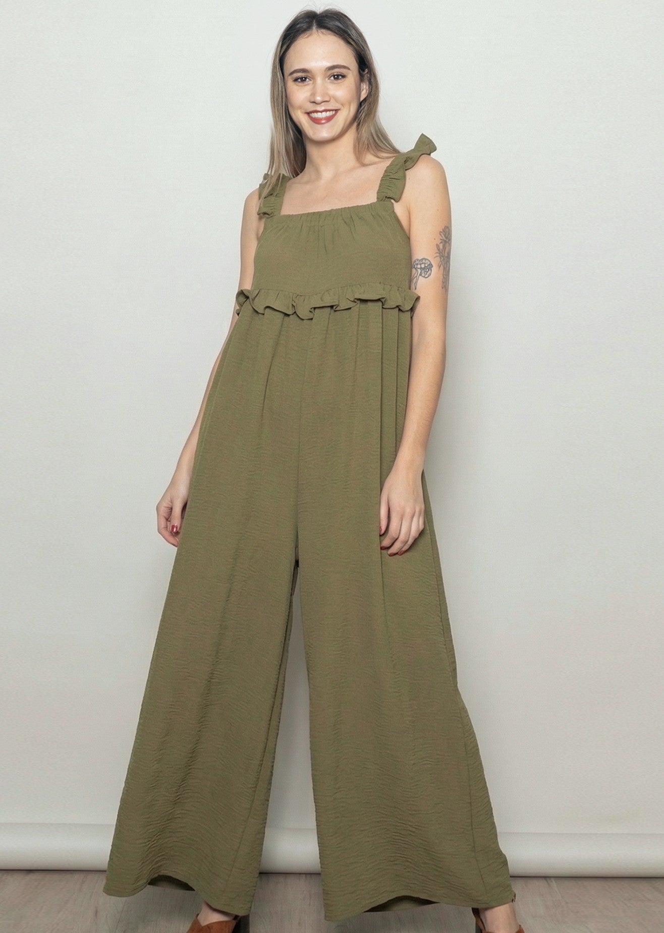 woman wearing an olive green ruffled jumpsuit with wide legs and adjustable straps