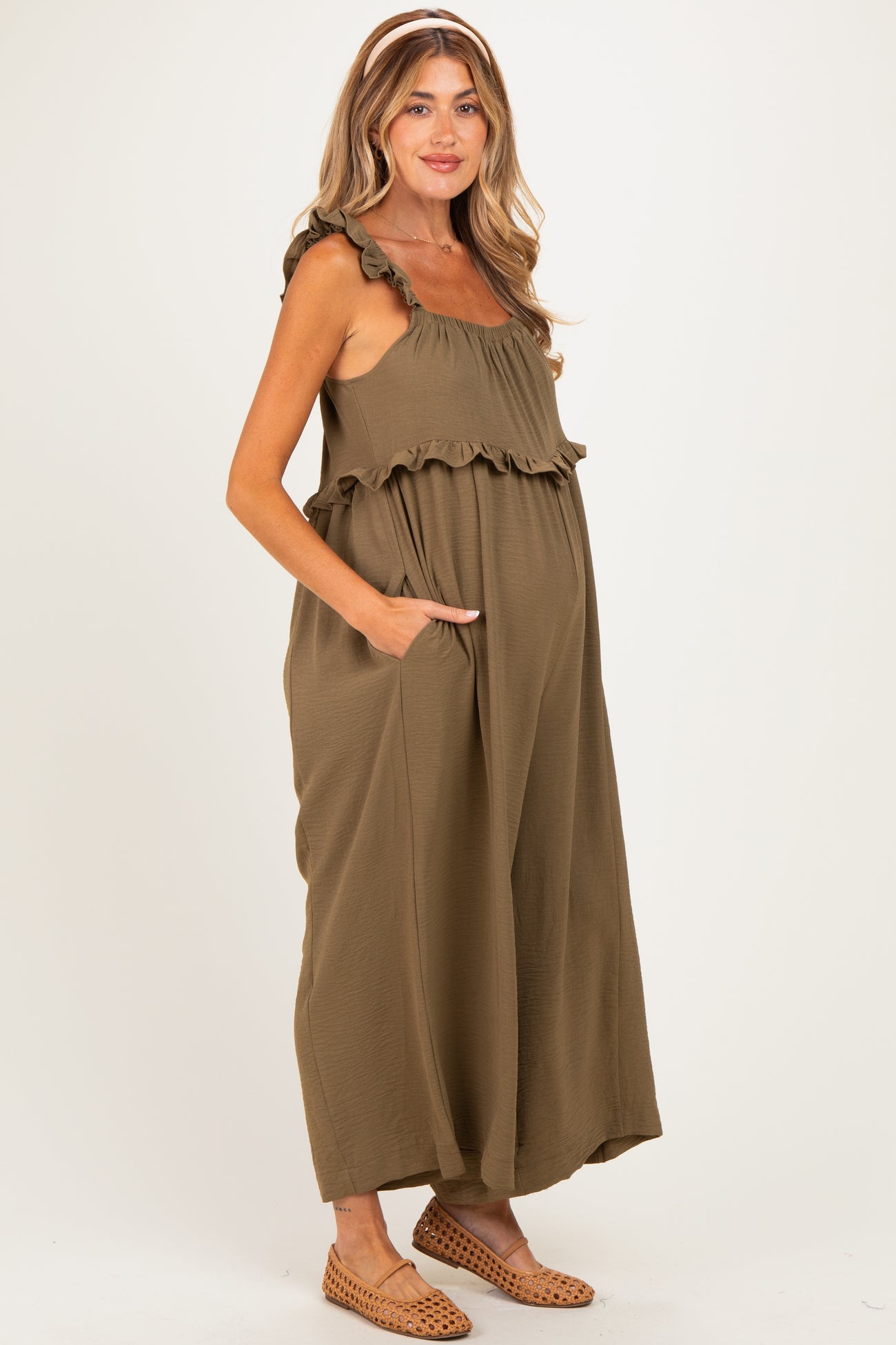 woman wearing an olive green maternity maxi dress with ruffle details and pockets, showing her baby bump