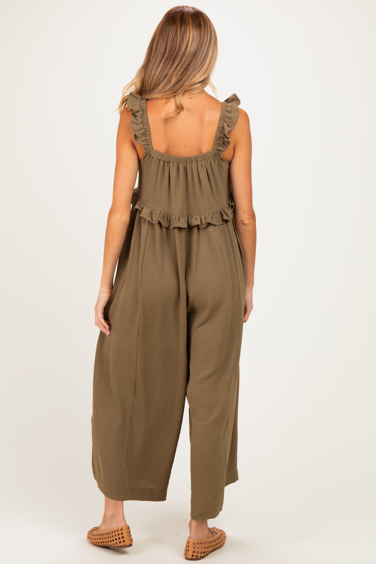 woman wearing a khaki green maternity jumpsuit with ruffle details on the straps and a loose fit