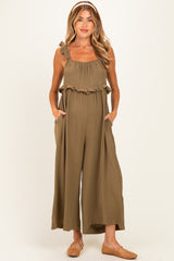 woman wearing a khaki green maternity jumpsuit with ruffle details and pockets, showing her baby bump